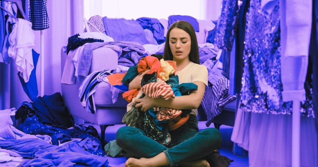 Une jeune femme assise au milieu d'une montagne de vêtements, victimes de la fast-fashion et de la société de consommation