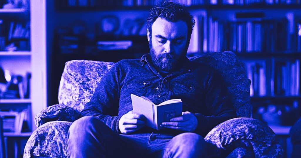 Un homme barbu assis dans un canapé lit un carnet