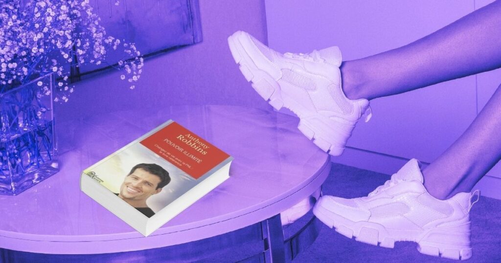 Une femme pose ses deux baskets blanche sur une table où est posé le livre "Pouvoir illimité" de Anthony Robbins