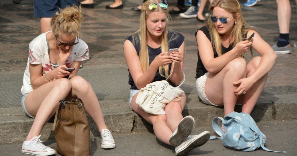 Trois jeunes filles assises sur un trottoir et consultant leurs smartphones