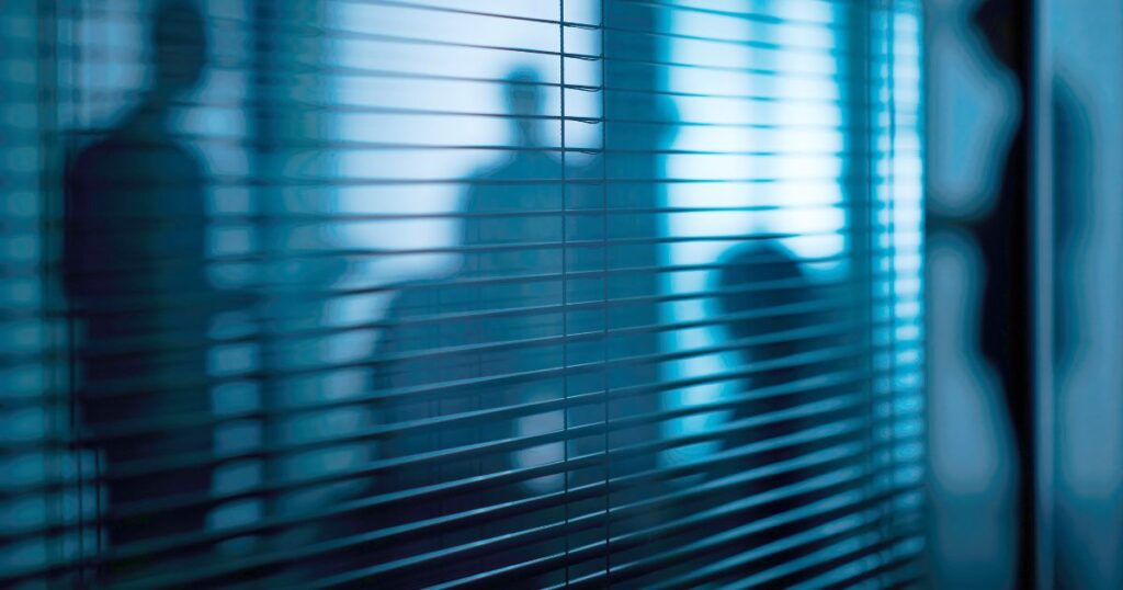 Silhouettes floues à travers des stores dans un bureau à lumières froides