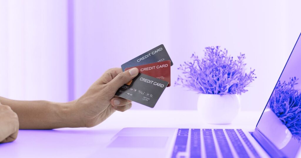 Une main tient trois cartes bleues devant un ordinateur portable