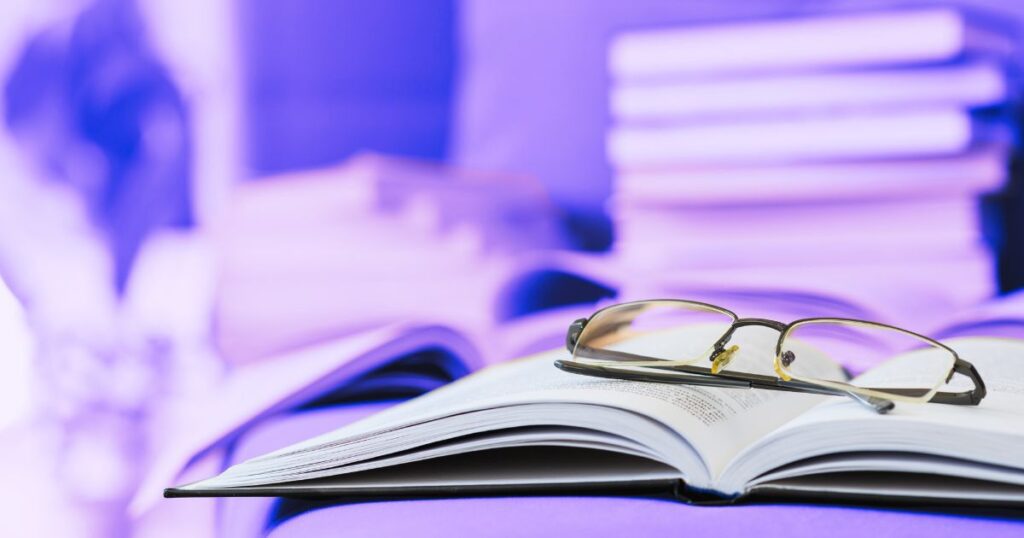 Une paire de lunettes posée sur un livre ouvert, devant une pile de livres : les meilleurs outils intellectuels