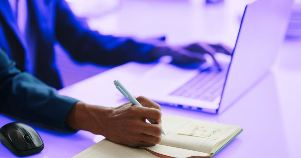 Une personne écrit sur un carnet de la main droite, pendant que la main gauche pianote sur un ordinateur portable, symbolisant l'engagement pour activer la curiosité
