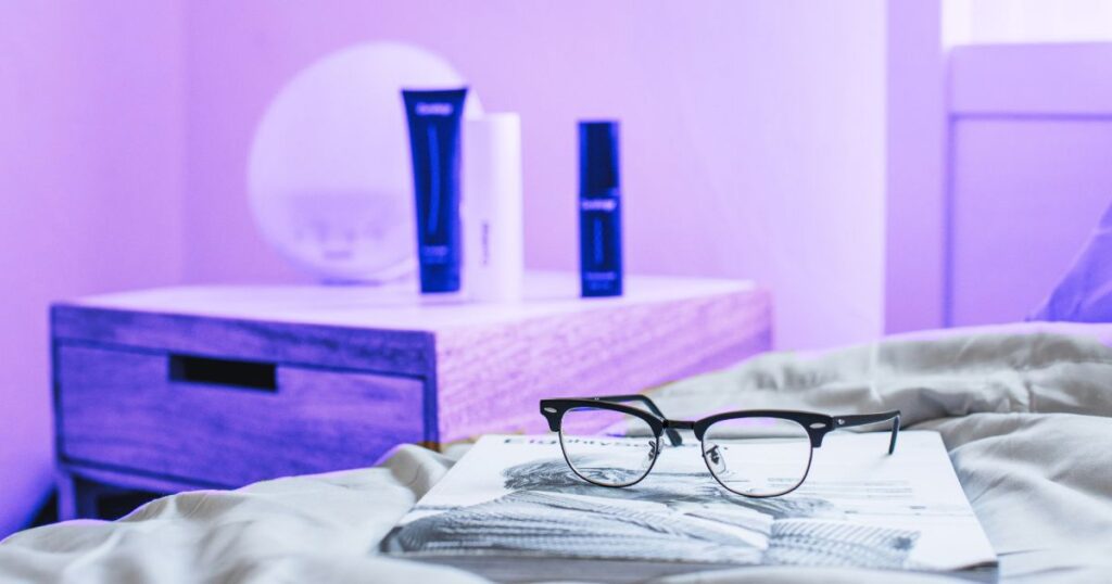 Une paire de lunettes et un journal posés sur un lit, avec une table de chevet en arrière-plan