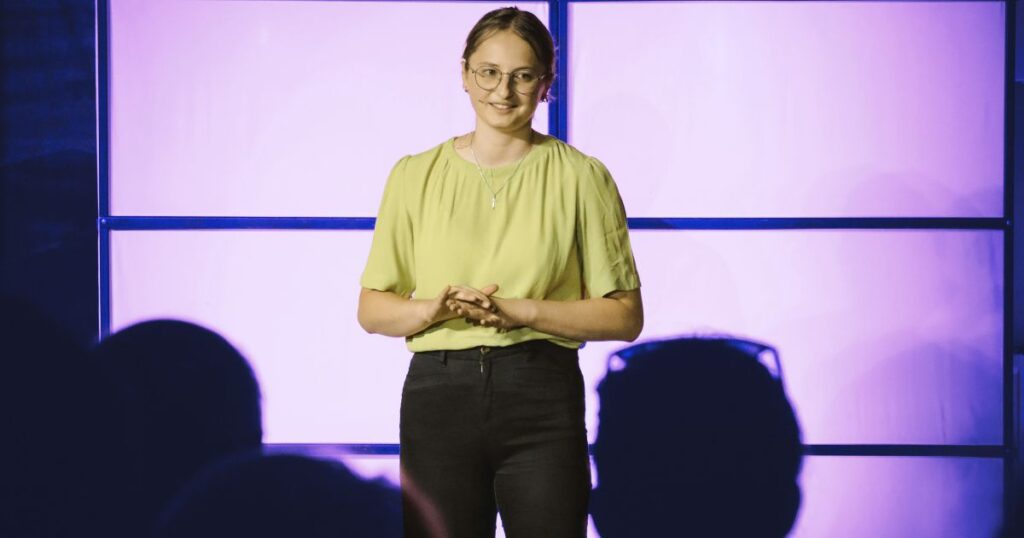 Oratrice souriante face à son audience, incarnant la personne cultivée