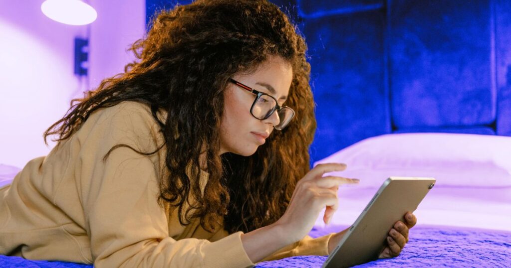 Une femme à lunettes consulte une tablette sur son lit, pour améliorer sa conversation par la culture
