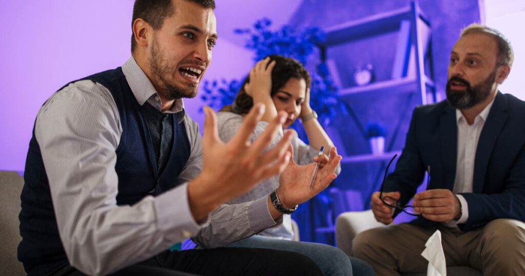 Un homme crie avec les mains ouvertes, tandis qu'une femme se bouche les oreilles et qu'un autre homme tente d'apaiser la situation