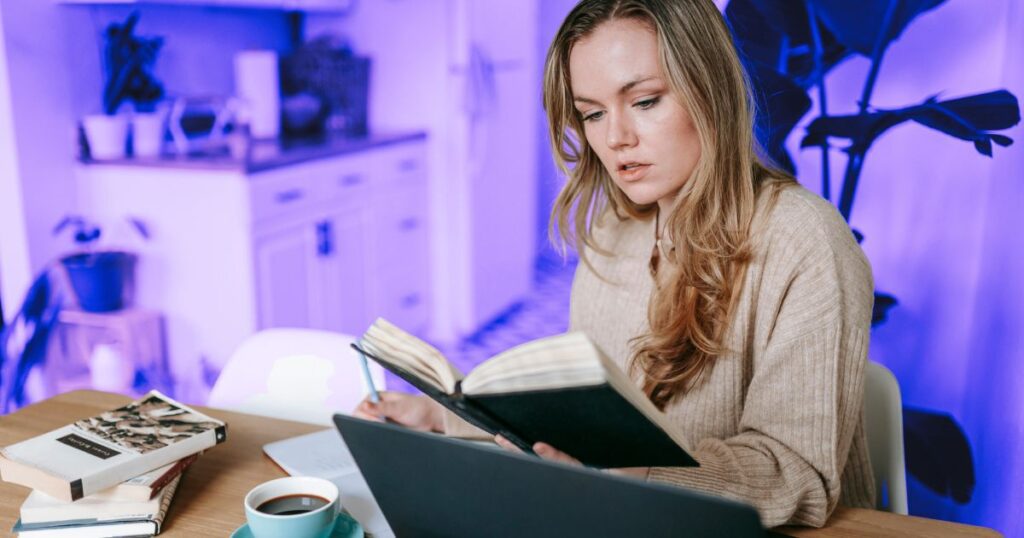 Une femme relit son carnet devant son ordinateur et une tasse de café