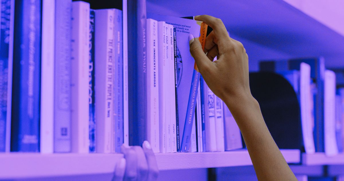 Une main sélectionne un livre sur une étagère dans une médiathèque