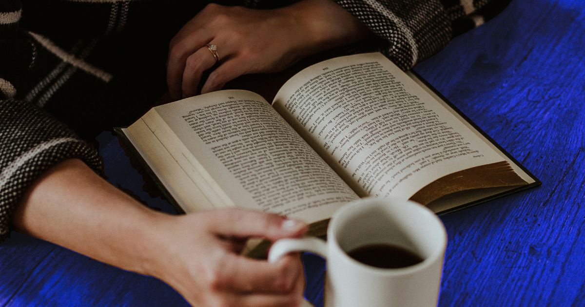 Gros plan sur un livre ouvert et une main qui tient une tasse de café