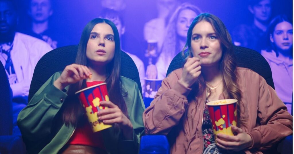 Deux jeunes femmes mangent du pop-corn dans une salle de cinéma, captivées par un film culte ou un grand classique