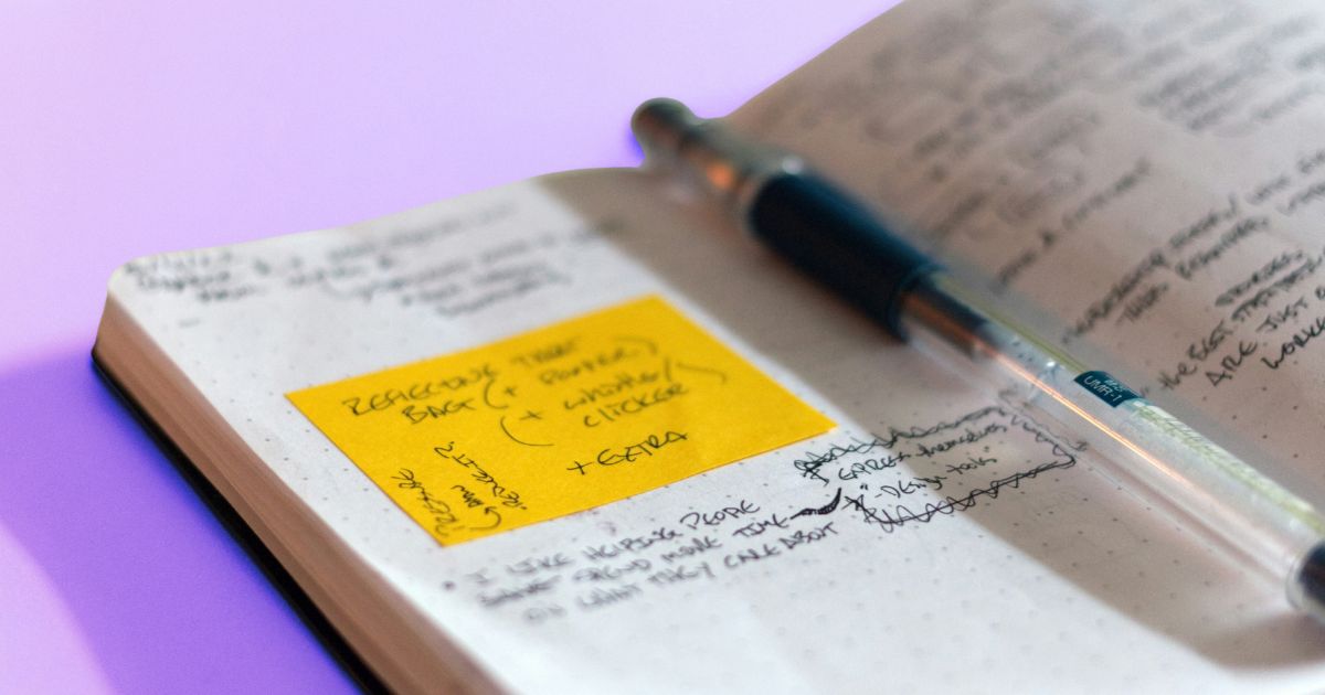 Un stylo est posé sur un livre ouvert avec un post-it jaune posé sur la page de gauche