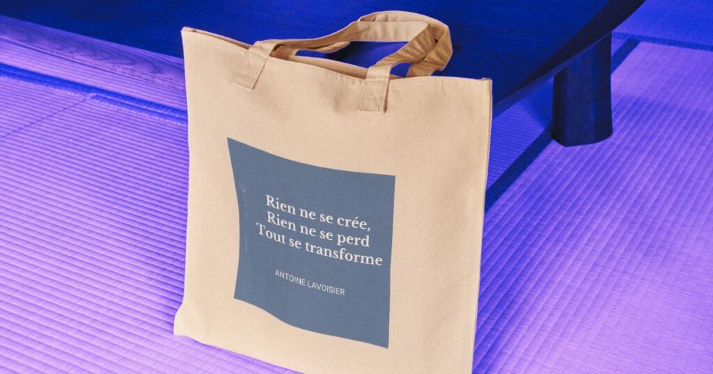 Un tote-bag avec une citation d'Antoine Lavoisier posé sur un tapis à côté d'un meuble